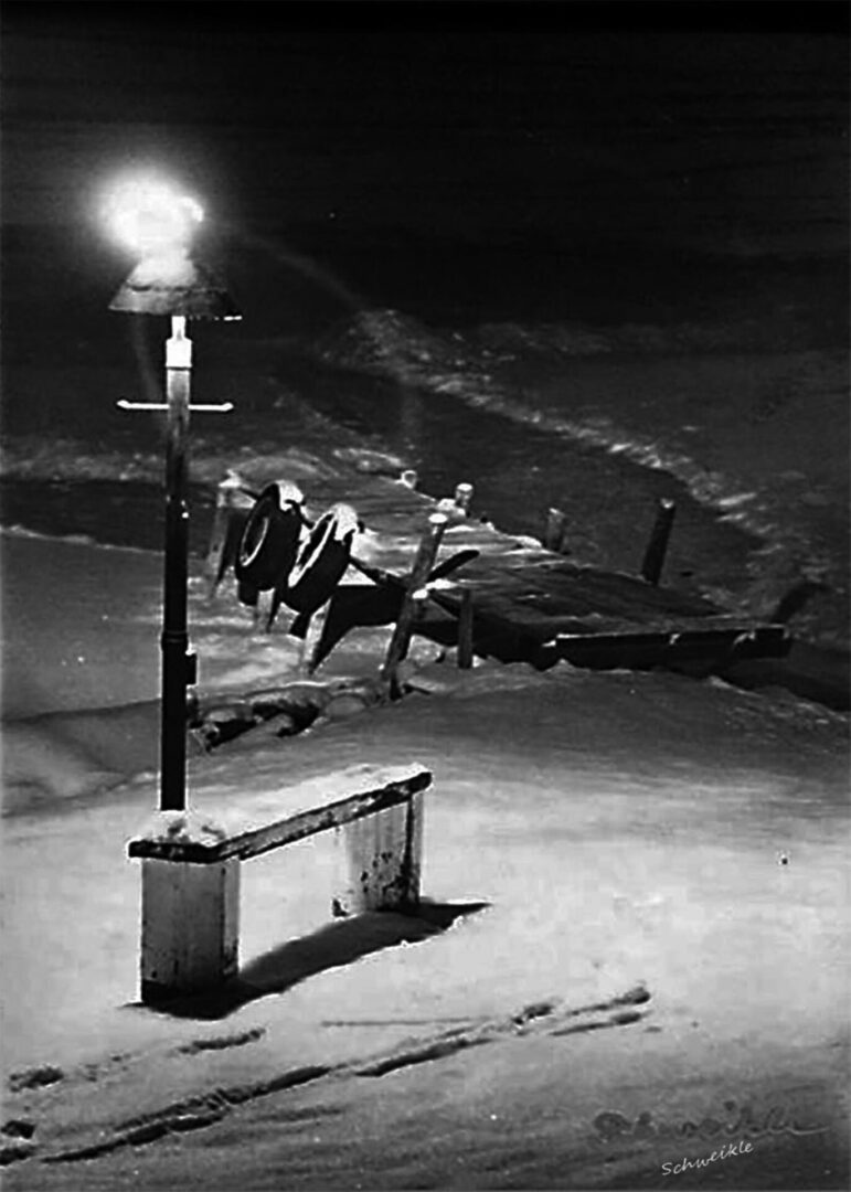 A black and white photo of a bench in the snow.